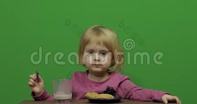女孩坐在桌子旁吃巧克力、<strong>饼干和饮料</strong>可可。 快乐的三岁女孩。 可爱的女孩微笑